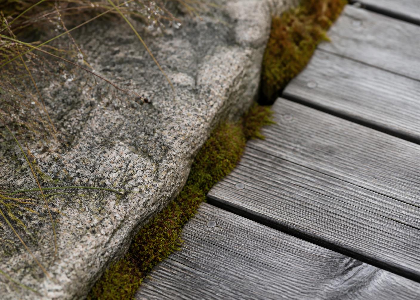 Detalj av granitkant mot obehandlat trädäck med mossa i fogen